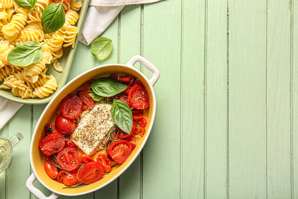 Baking dish with tasty tomatoes, feta cheese and pasta on green wooden background - Photo, Image