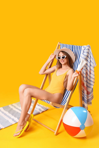 Mujer joven con crema protector solar sentada en la silla de cubierta sobre fondo amarillo - Foto, imagen