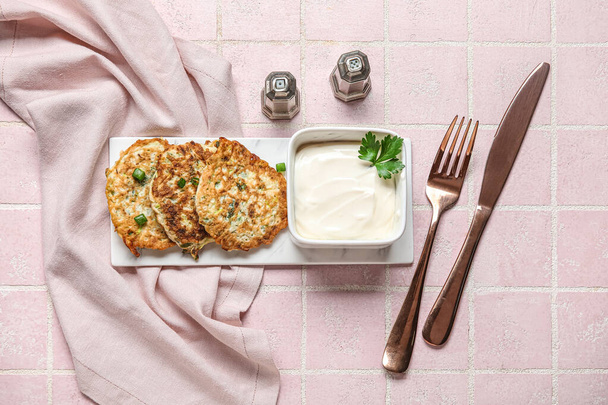 Board of tasty zucchini fritters with sour cream on pink tile background - Photo, Image