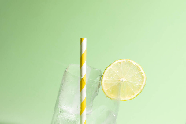 Cold glass full of ice with a slice of lime and a striped yellow and white straw - Photo, image