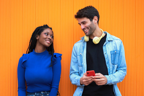 Többnemzetiségű pár nézi egymást, miközben fejhallgatót és mobiltelefont használnak. Technológia és kapcsolatrendszer. - Fotó, kép