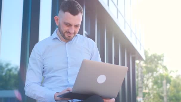 A young business freelancer works with a laptop on the street near an office center. Young business man - Video