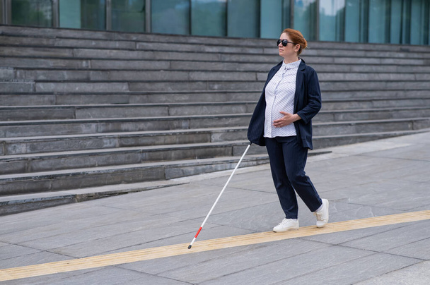 Blind pregnant businesswoman walking along tactile tiles with a cane - Foto, afbeelding