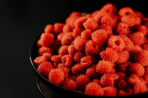Fresh, ripe, juicy raspberry background, close up berry . Food background. Gastronomy concept, organic food. Macro red raspberries fruit in plate on black background - Photo, Image