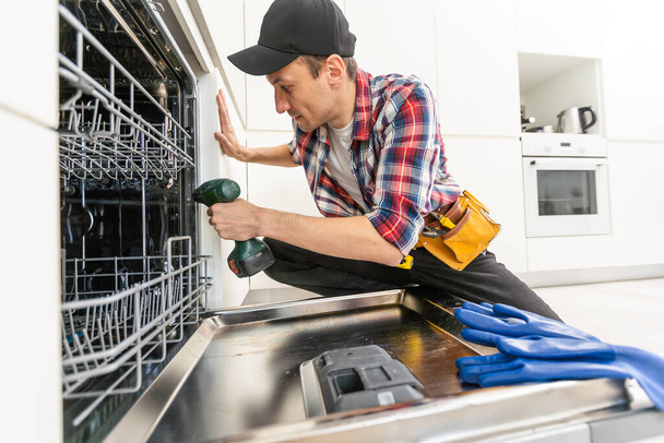 Trabajador usando destornillador para reparar lavavajillas en casa foto de stock. Foto de alta calidad - Foto, Imagen