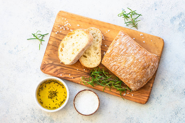 Ciabatta bread on wooden board with olive oil. Top view on white table. - Photo, Image