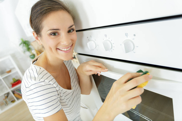 a happy woman is cleaning the oven - Foto, afbeelding