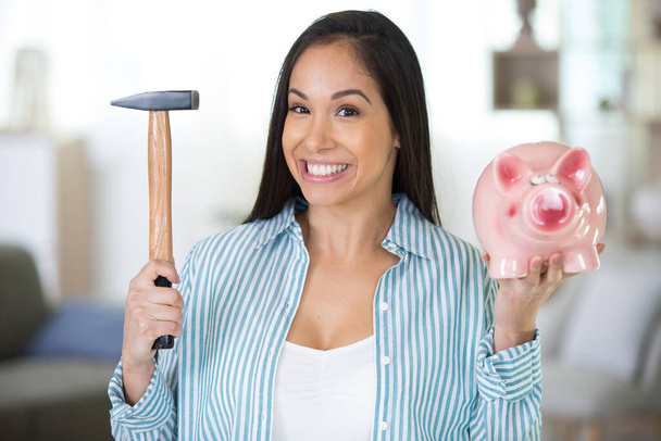 smiling woman in casual clothing breaking moneybox with hammer - Foto, Imagen