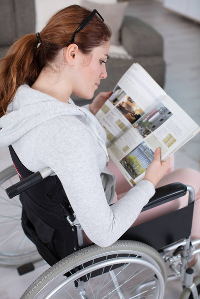 good-looking disabled woman sitting in a wheelchair holding a magazine - Фото, изображение