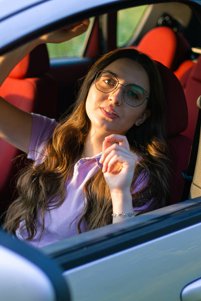 young woman in a new car in a summer day.serious woman in the car.Driving a car as a hobby.Renting a car.confident woman driving.emotional girl in the auto.holding the steering wheel.woman with car.upset girl.portrait.girl dreams.deep look.beautiful  - Фото, изображение