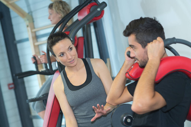 young female coach assisting man using fly machine in gym - Foto, afbeelding