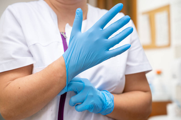 Close up de uma enfermeira colocando uma luvas de látex azul em um fundo de clínica. Foto de alta qualidade - Foto, Imagem