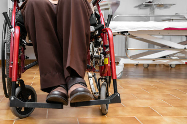 Ανώτερη ασθενής σε αναπηρική καρέκλα στην κλινική φυσιοθεραπείας αποκατάστασης ή στο ιατρείο, αγνώριστη ηλικιωμένη γυναίκα. Υψηλής ποιότητας φωτογραφία. Υψηλής ποιότητας φωτογραφία - Φωτογραφία, εικόνα