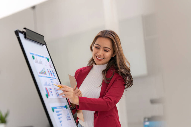 Kancelářská pracovnice pracující na její prezentaci stojící u bílé tabule finanční výkaz zisku. - Fotografie, Obrázek