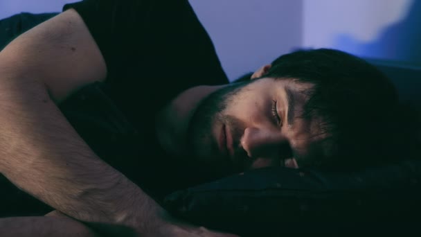 Ein Mann schläft in einem dunklen Raum und wacht auf, öffnet die Augen und steigt aus dem Bett. - Filmmaterial, Video