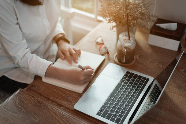Женщина в элегантной повседневной одежде пишет на ноутбуке и работает на ноутбуке, сидя в креативном офисе или кафе. молодая девушка работает с ноутбуком на деревянном столе в кафе - Фото, изображение