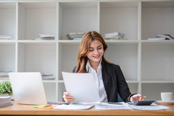 Азиатская деловая женщина в официальном деловом костюме использует свой ноутбук и работает над маркетинговыми отчетами за своим столом в офисе - Фото, изображение