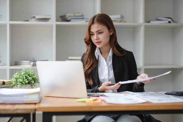 Mujer de negocios asiática en un traje de negocios formal está utilizando su computadora portátil y trabajando en informes de marketing en su escritorio en la oficina - Foto, imagen