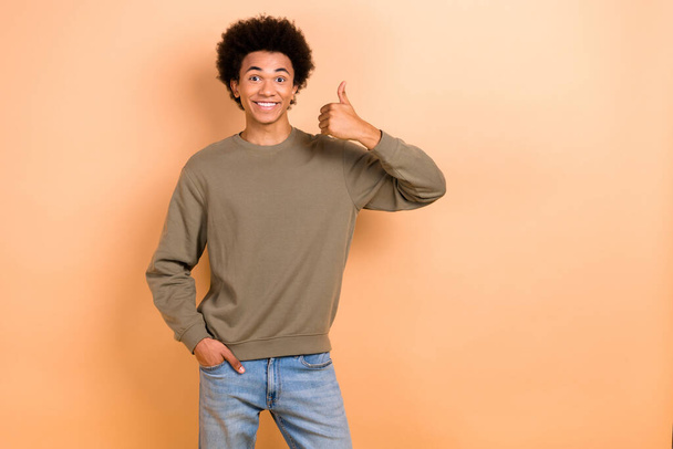 Photo of young optimistic guy chevelure hair thumb up wear stylish pullover thumb up like new clothes brand advert isolated on beige color background. - Foto, Bild