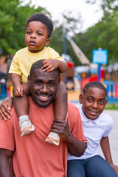 Портрет африканского чёрного отца с детьми на детской площадке городского парка - Фото, изображение