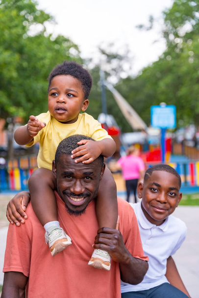 Portrait of African black ethnicity father smiling with his children at playground in city park - Foto, Bild