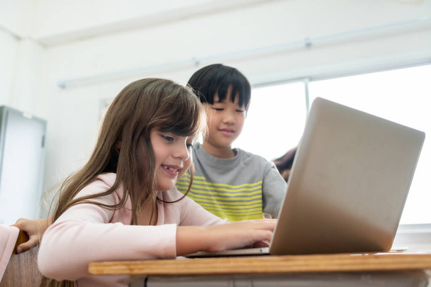 Счастливые двое слоновских школьников пользуются ноутбуком за партой в классной комнате в школе. - Фото, изображение