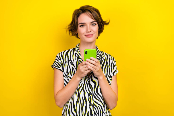Photo of cheerful adorable girl with bob hairdo dressed zebra print shirt hold smartphone read sms isolated on yellow color background. - Φωτογραφία, εικόνα