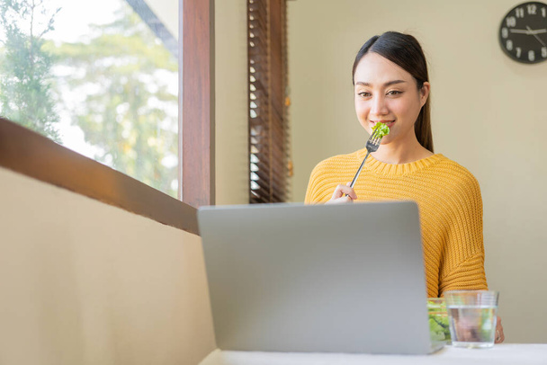 Happy young Asian woman with fresh vegetables and fresh fruits, healthy concept working lunch at home, beautiful woman with laptop eating salad, lifestyle in living room concept. - Foto, imagen