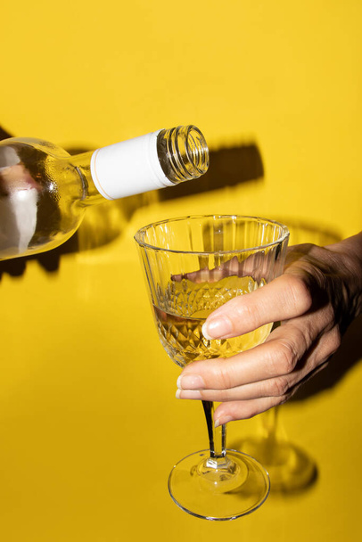 Weibliche Hände gießen Weißwein auf gelbem Hintergrund ein - Foto, Bild
