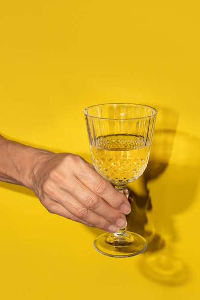 Mano sosteniendo el vino blanco en una copa sobre un fondo amarillo - Foto, imagen