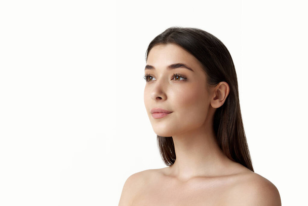 Portrait of attractive, young, brunette woman with bare shoulders, perfect well-kept face, looking straight over white studio background. Concept of female beauty, body and skincare, cosmetology, ad - 写真・画像