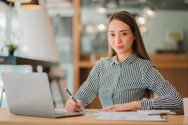 Азиатская деловая женщина в костюме сидит на столе в офисе, с графиком компьютерных документов для бухгалтерии на рабочем месте, чтобы рассчитать годовую прибыль по функциям, бизнес-концепции - Фото, изображение
