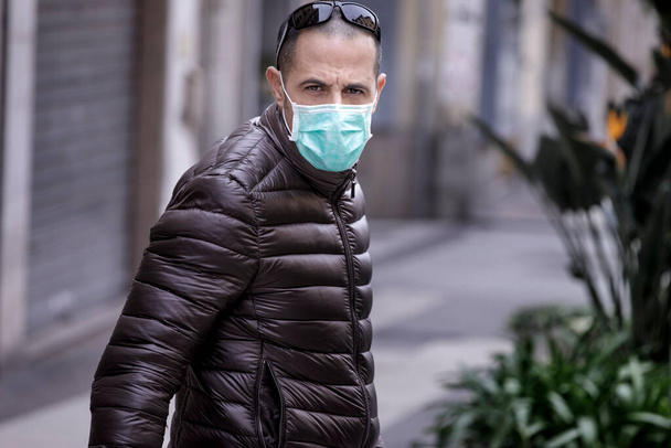 Чоловік з масками та коричневою курткою ходить по безлюдній вулиці італійського міста. - Фото, зображення