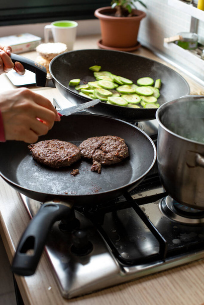 Hamburgers cooked in a frying pan over a kitchen stove and checked by a cook so as not to burn - Photo, image