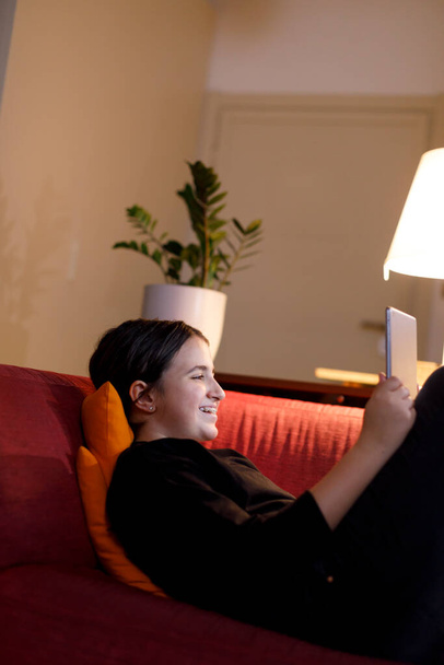 nastolatka z ciemnymi włosami patrząc na tablet leżący wygodnie w domu - Zdjęcie, obraz