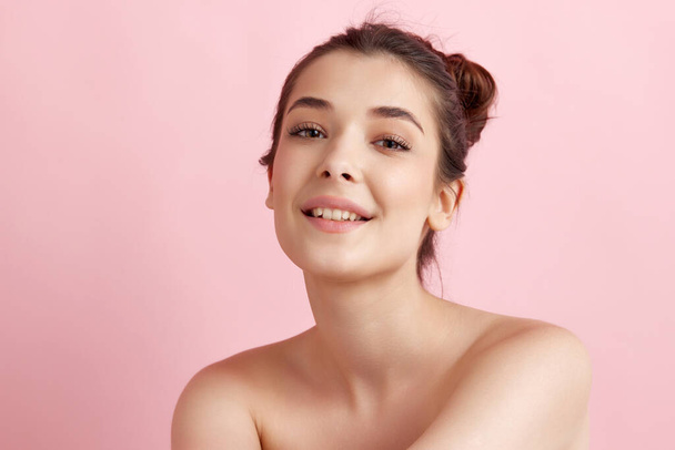 Tender, beautiful young woman with bare shoulders, well-kept, smooth, healthy skin looking at camera over pink background. Concept of natural female beauty, body and skincare, cosmetology, health, ad - Foto, afbeelding