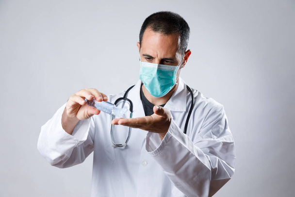 Beyaz önlüklü ve maskeli bir doktor beyaz arka planda izole edilmiş antibakteriyel jelle ellerini dezenfekte ediyor. - Fotoğraf, Görsel