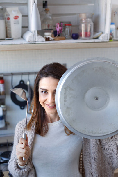 молодая женщина с металлическим горшком в руках на кухне  - Фото, изображение