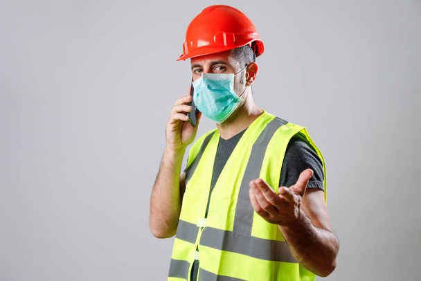 worker with protective helmet, face mask and gillet speaks on phone - Foto, Bild