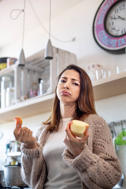 μελαχρινή κοπέλα σνιφάρει στην κουζίνα ενώ τρώει ένα μήλο - Φωτογραφία, εικόνα