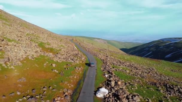 Car moves along road, making its way high in snow-capped mountains of Armenia. Drone photography captures majestic landscapes: icy rocks, drone deftly follows car, conveying atmosphere of adventure - Footage, Video