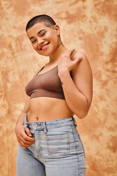 body love, jeans look, curvy and tattooed woman in casual attire standing on mottled beige background, confidence, self-acceptance, generation z, body diversity, pretty and positive  - Фото, зображення