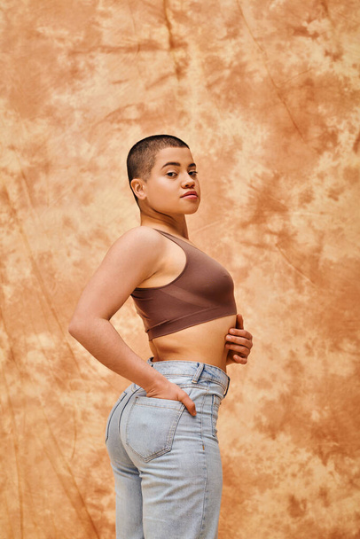 denim fashion, gen z, young curvy woman posing on mottled beige background, different shapes, body positivity movement, self-esteem, confidence, short haired model, hand in pocket - Фото, зображення