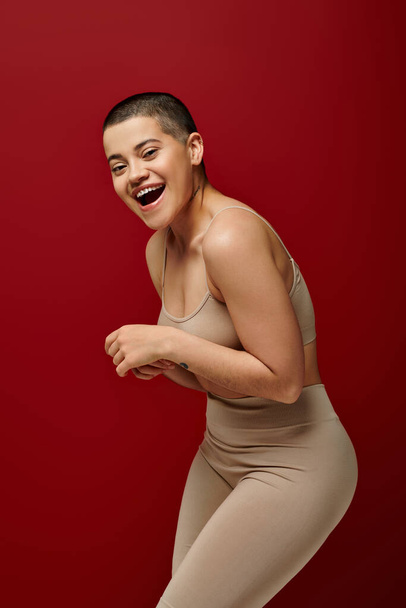 self-esteem, happy and tattooed woman in beige underwear posing on red background, curvy fashion, comfortable in skin, body positivity, generation z, body diversity, laughter, joy  - Фото, изображение