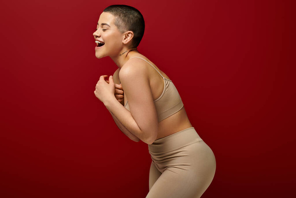 self-esteem, happy and tattooed woman in beige underwear posing on red background, curvy fashion, comfortable in skin, body positivity, generation z, body diversity, laughter, joy  - Фото, изображение