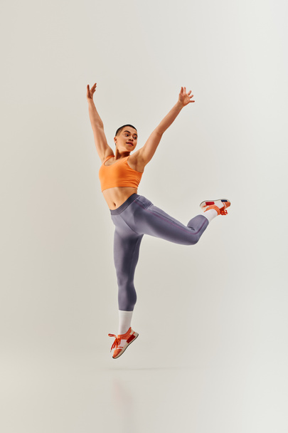 body positivity movement, young curvy and short haired woman jumping on grey background, female fitness, empowerment, motivation, working out, sportswear, strength and health, body image  - Photo, Image