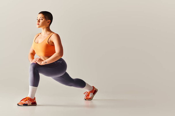 body positivity movement, young short haired woman doing lunges on grey background, curvy fitness model in sportswear, empowerment, motivation, working out, strength and health  - Fotó, kép