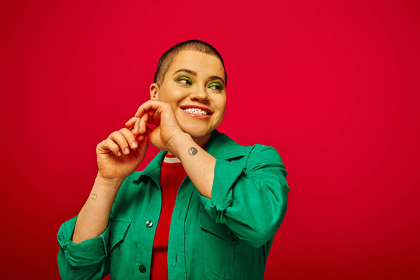 fashion and style, cheerful and short haired woman in green outfit posing with raised hands on red background, generation z, youth culture, modern backdrop, individuality, personal style  - Photo, Image