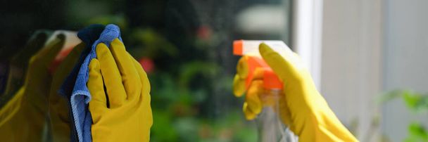 Close-up of female hands cleaning window outside using detergent spray and rag. House cleaning, housekeeping and spring-cleaning concept - Fotoğraf, Görsel