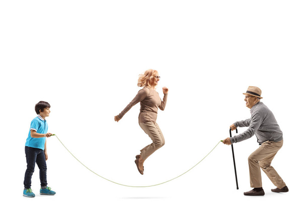 Full length profile shot of a grandfather and grandson holding a rope and an woman skipping isolated on white background - Photo, image